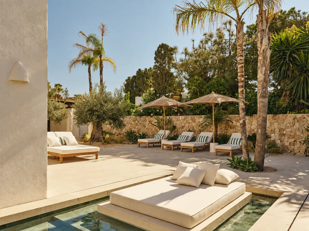 Piscina con camas balinesas y palmeras en un jardín soleado